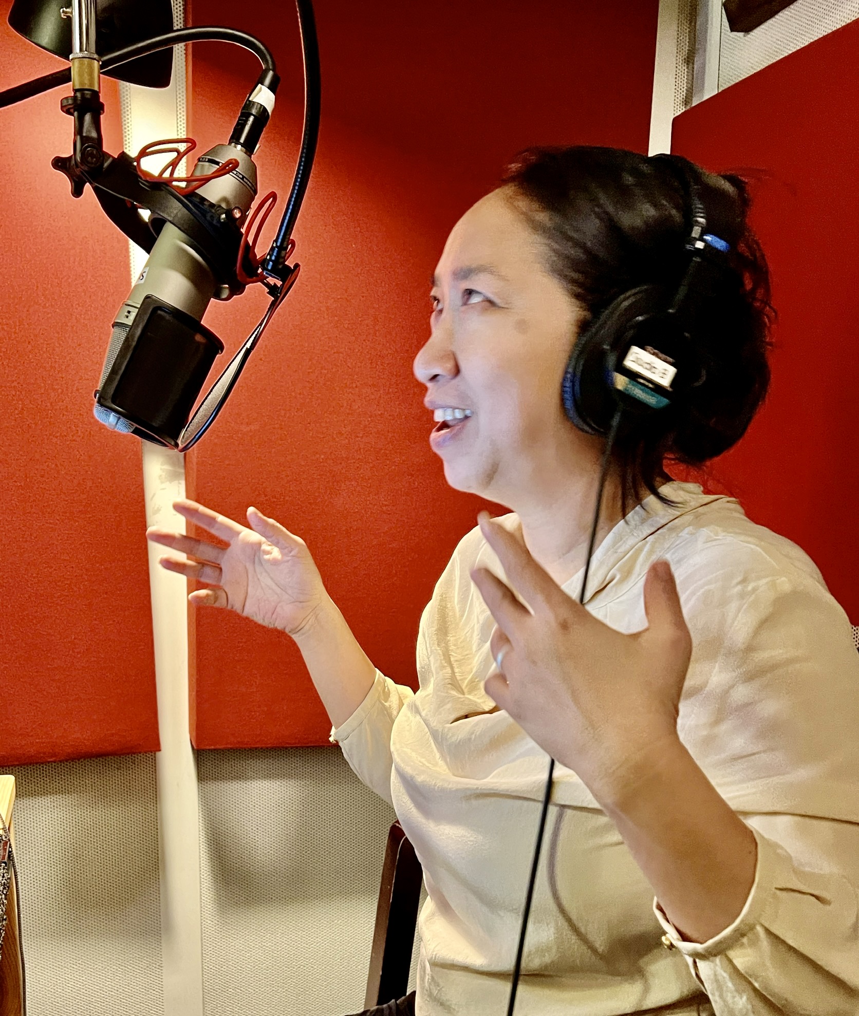 Author in studio, wearing headphones, speaks into a microphone
